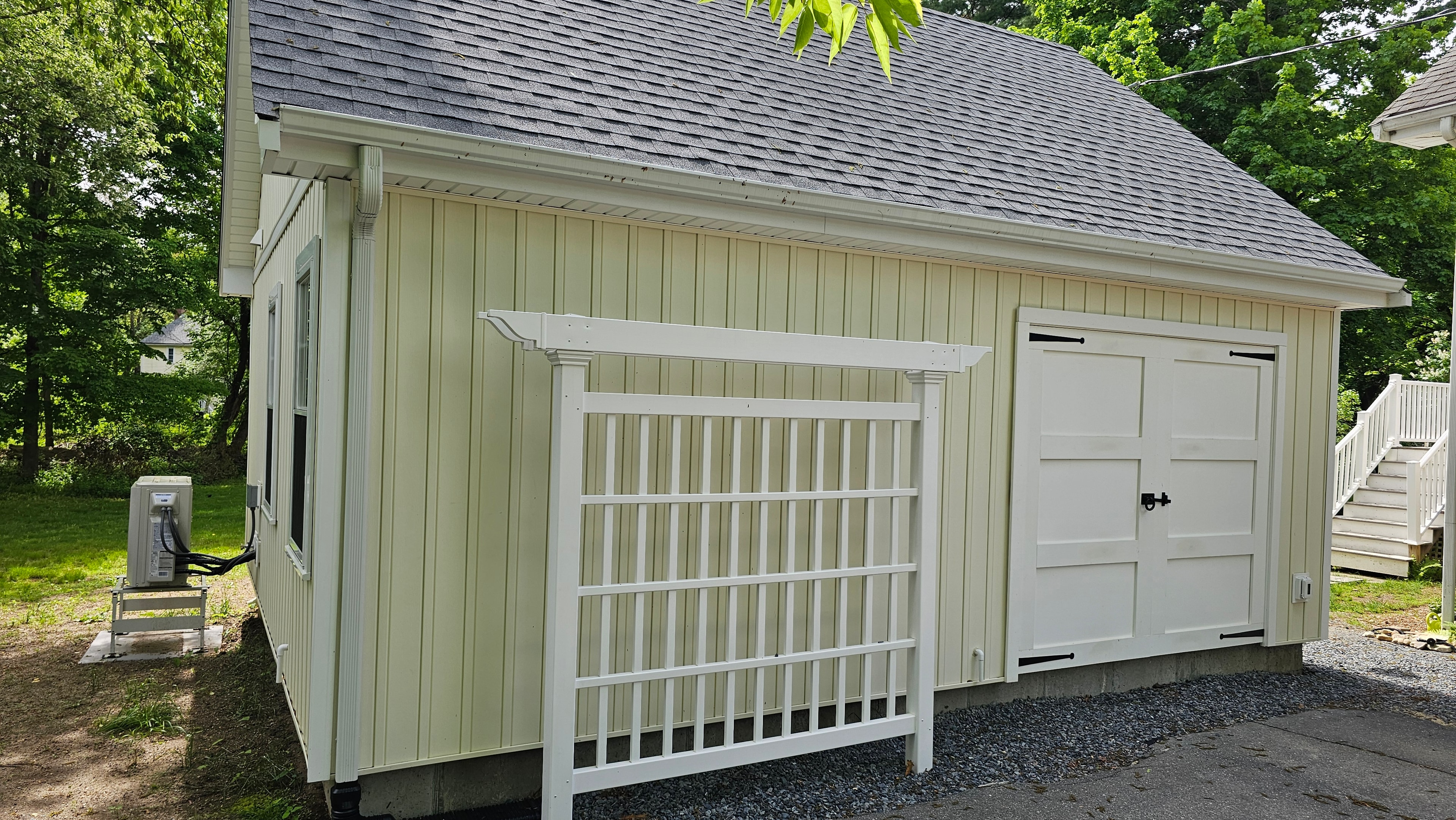 Exterior of the Medway ADU showing white paneled doors with black hardware, board-and-batten siding, white trim, and a trellis structure.