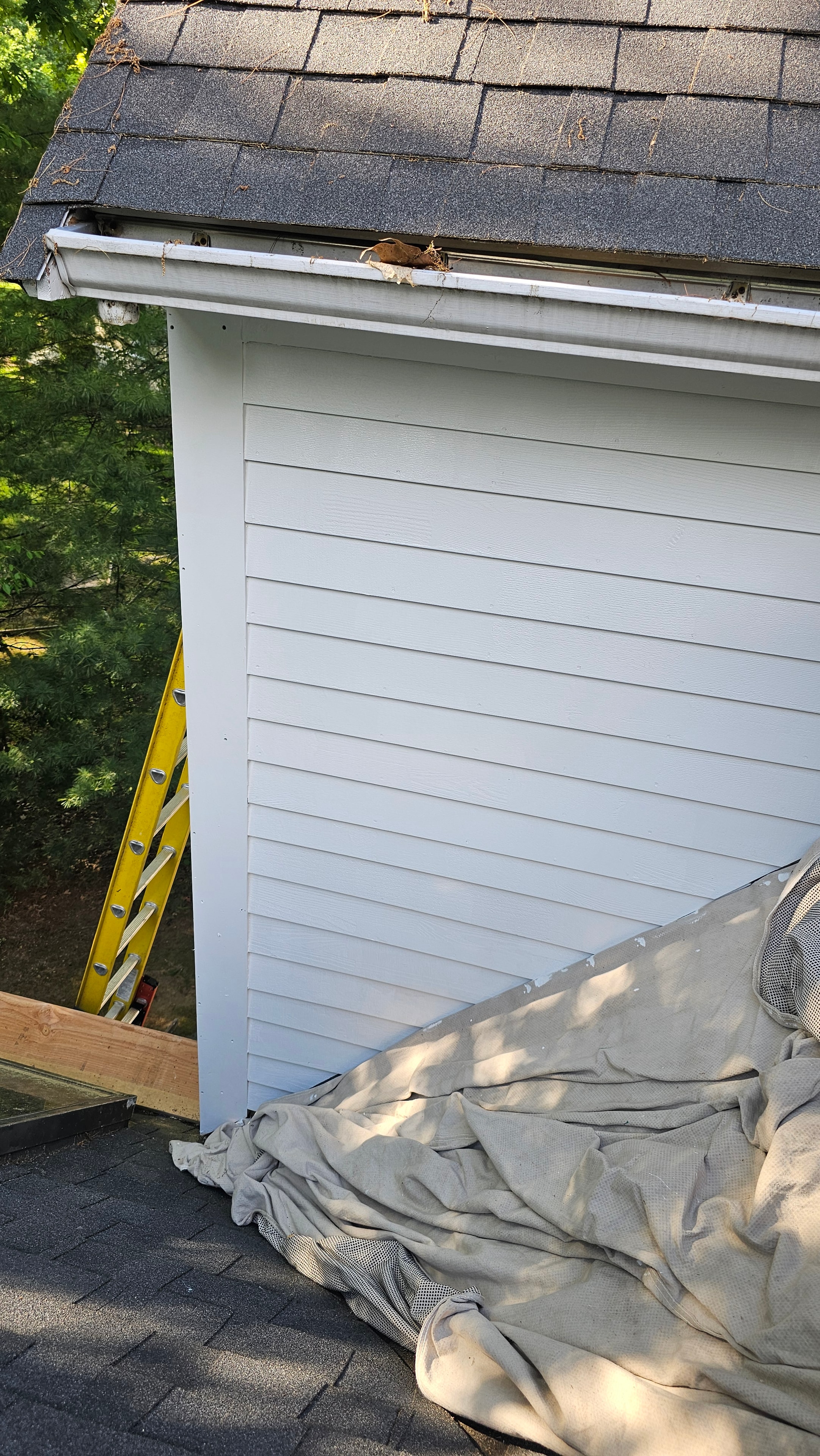 Overhead view of the completed rear siding on the Natick property — new white board-and-batten siding, gutter, and drop cloth on the ground below.