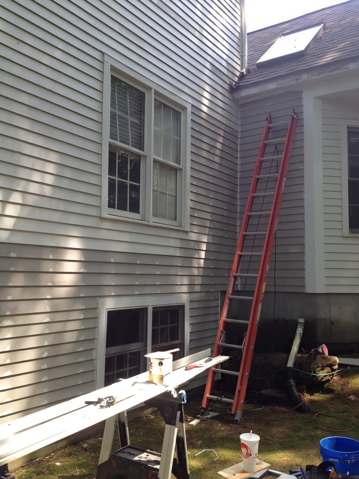 Rear elevation of the Natick property during the restoration, showing the original gray siding, an orange ladder, and a work table with tools.