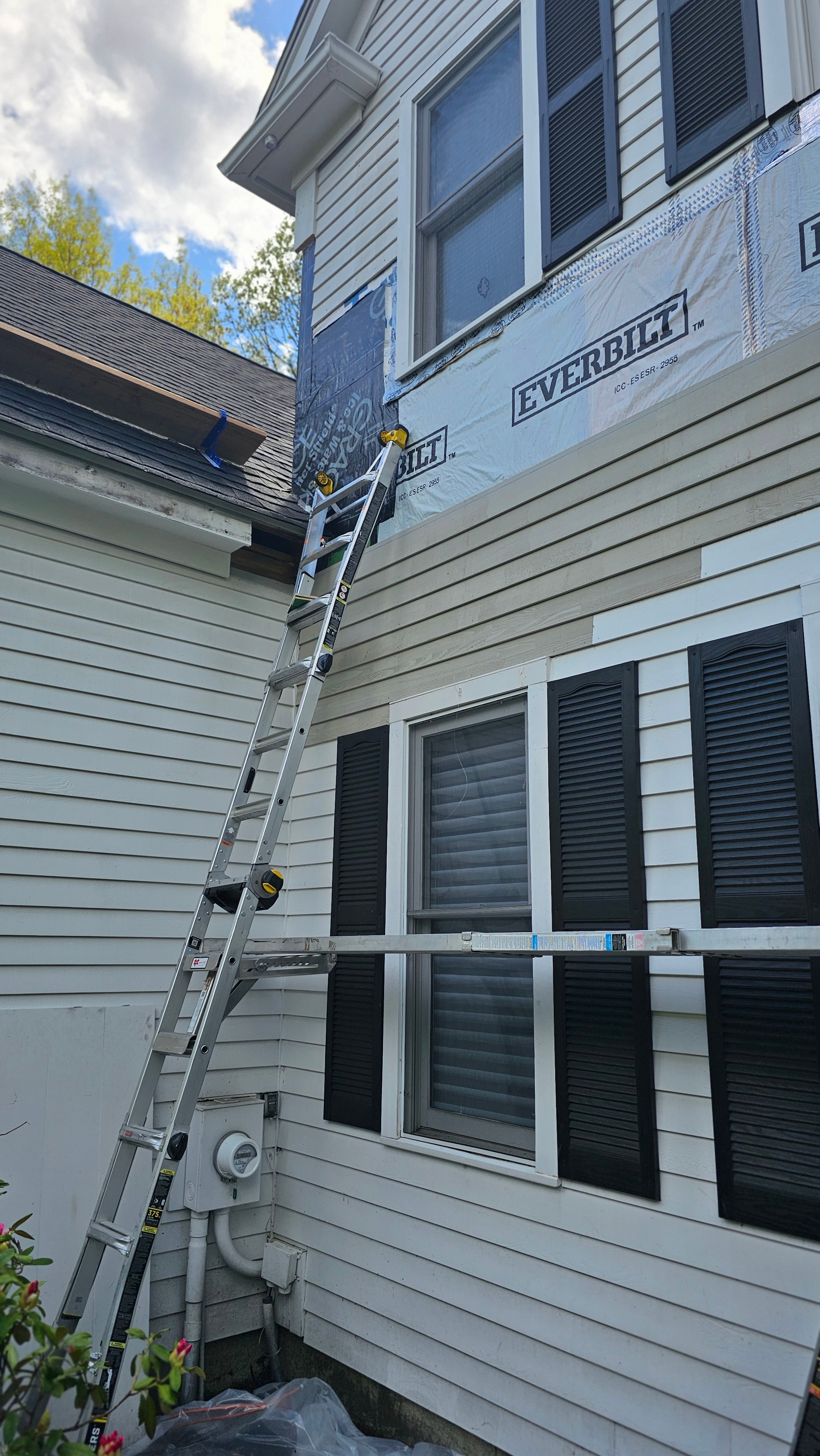 New siding panels being installed on the Natick exterior restoration, with two ladders against the wall and ice-and-water barrier visible at the base.