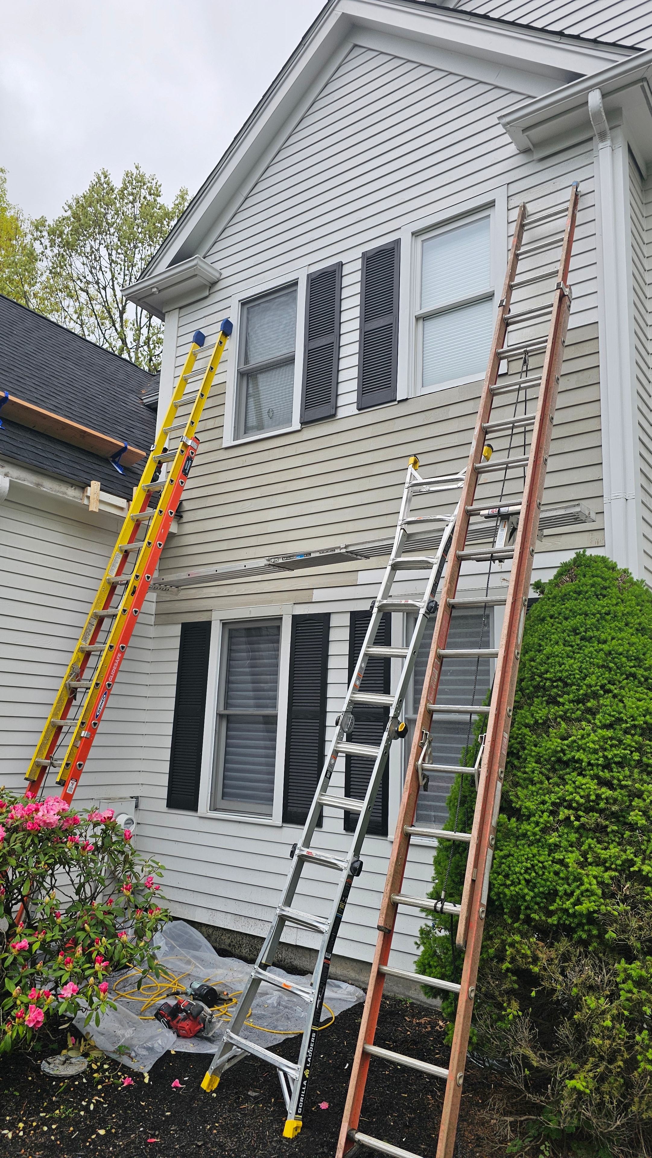 Ladders leaning against the Natick house exterior during siding restoration work, showing the project in progress across multiple areas.