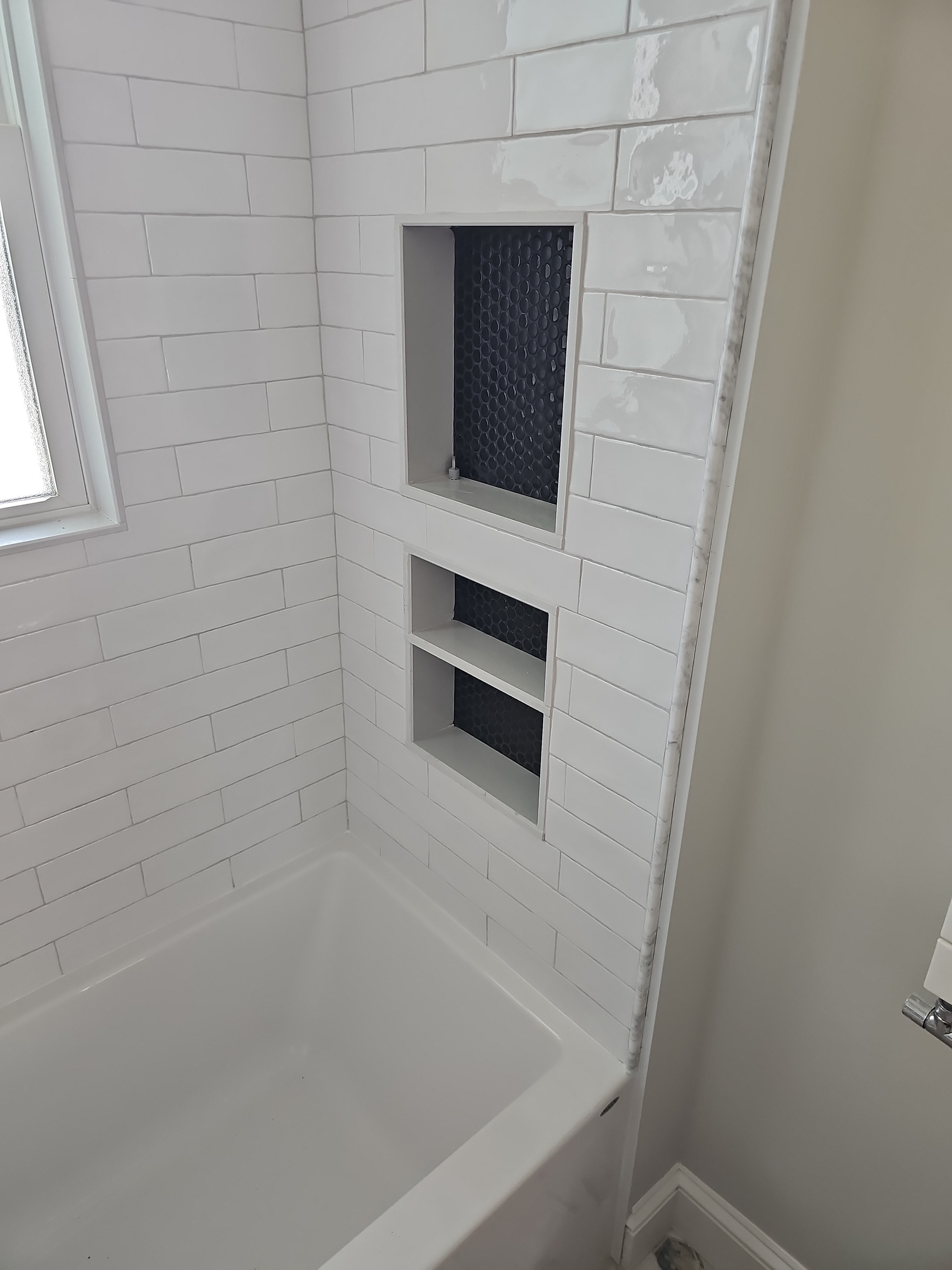 Custom triple shower niche — white subway tile with black hex tile backing and marble threshold