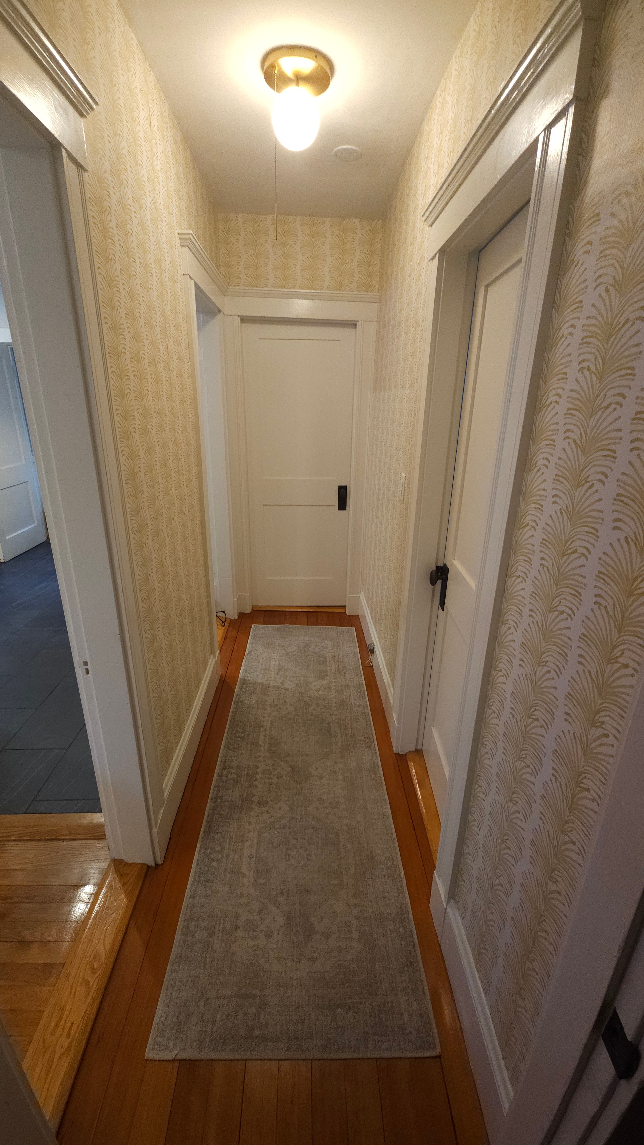 Hallway after — gold botanical wallpaper, coffered ceiling, brass sconce, wood floor